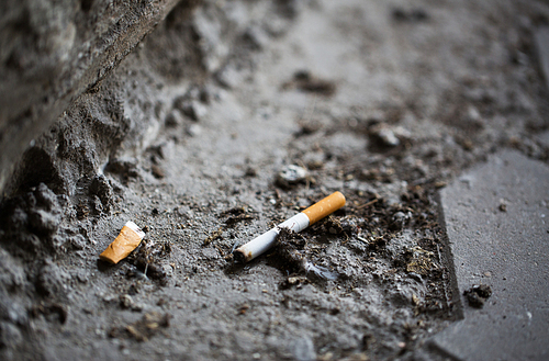 smoking, substance abuse, addiction, people and bad habits concept - close up of smoked cigarette butt on ground