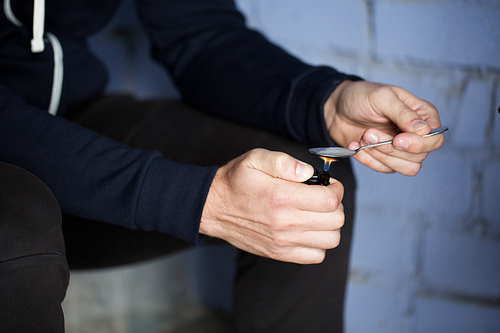 drug use, crime, addiction, substance abuse and people concept - close up of addict with lighter and spoon preparing dose of crack cocaine on street