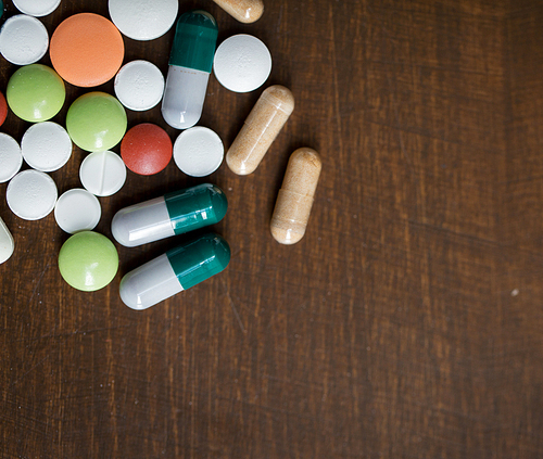 addiction, medication, medicine and substance abuse concept - close up of different drugs in pills and capsules on table