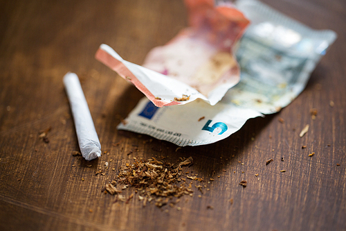 substance abuse, nicotine addiction, drug sale and smoking concept - close up of marijuana joint and money