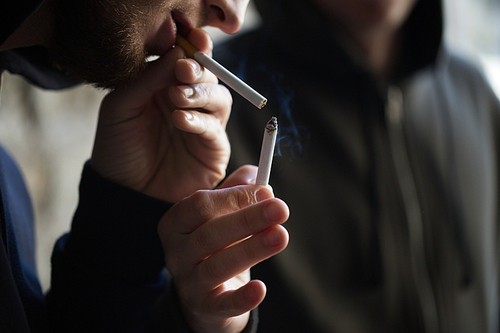 smoking, substance abuse, addiction and bad habits concept - close up of young people lighting cigarette outdoors