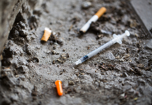 smoking, substance abuse, addiction and drug use concept - close up of syringe and smoked cigarette on ground