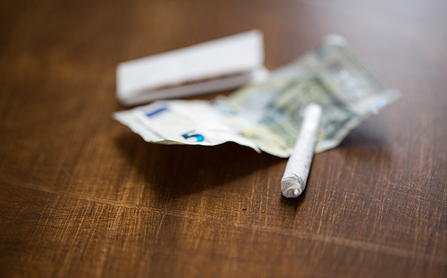 substance abuse, nicotine addiction, drug sale and smoking concept - close up of marijuana joint and money