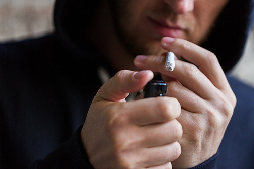 drug use, substance abuse, addiction, people and smoking concept - close up of addict lighting up marijuana joint with lighter