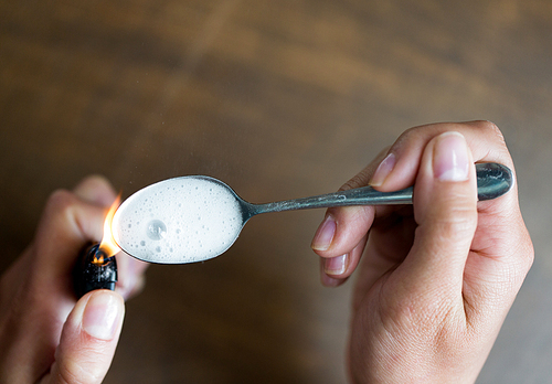 drug use, crime, addiction, substance abuse and people concept - close up of addict hands with lighter and spoon preparing dose of crack cocaine on street