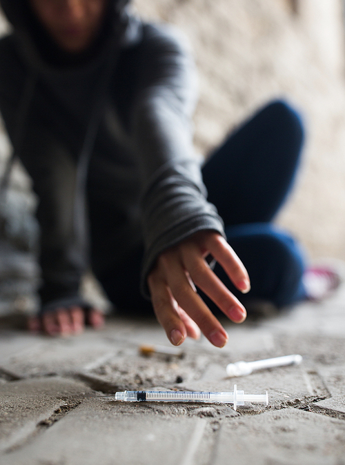 substance abuse, addiction, people and drug use concept - close up of addict woman reaching to used syringes on ground