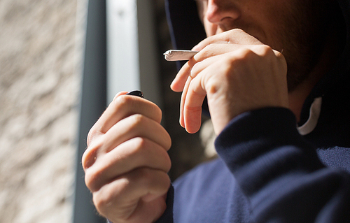 drug use, substance abuse, addiction, smoking and people concept - close up of addict hands with marijuana joint and lighter