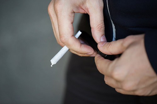 drug use, substance abuse, addiction, people and smoking concept - close up of addict hands with marijuana joint and lighter