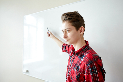 education, school, learning and people concept - student boy with marker showing something on blank white board