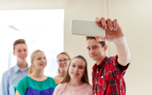 education, high school, technology and people concept - group of happy smiling students taking selfie picture with smartphone in corridor