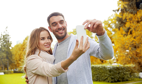 love, relationship, technology and people concept - happy couple with smartphone taking selfie in autumn city park