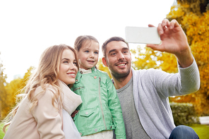 family, childhood, technology and people concept - happy father, mother and little daughter taking selfie by smartphone in autumn park