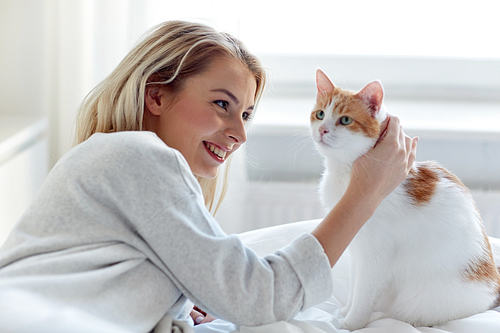 pets, morning, comfort, rest and people concept - happy young woman with cat in bed at home