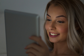 technology, internet, communication and people concept - happy smiling young woman with tablet pc computer in bed at home bedroom at night