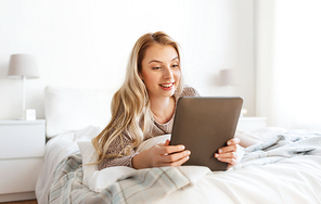 technology, internet and people concept - happy young woman lying in bed with tablet pc computer at home bedroom