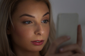 technology, internet, communication and people concept - young woman texting on smartphone at home at night