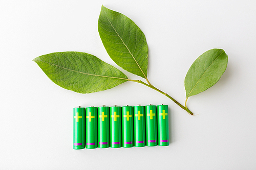 recycling, energy, power, environment and ecology concept - close up of green alkaline batteries and leaf