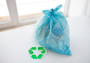 waste recycling, reuse, garbage disposal, environment and ecology concept - close up of rubbish bag with trash or garbage and green recycle symbol at home