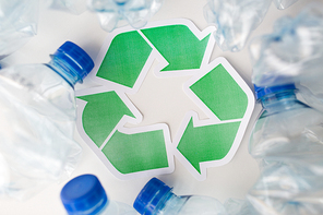 waste recycling, reuse, garbage disposal, environment and ecology concept - close up of used plastic water bottles with green recycle symbol on table