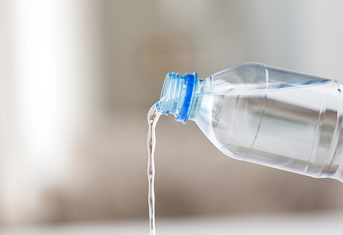 drinking, healthy eating and food storage concept - close up of water pouring from plastic bottle