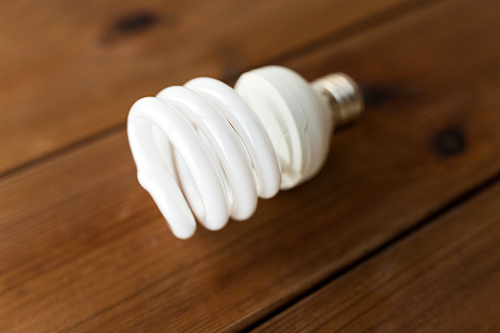 recycling, electricity, environment and ecology concept - close up of energy saving lighting bulb on wooden boards