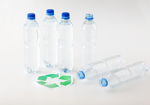 recycling, reuse, garbage disposal, environment and ecology concept - close up of plastic water bottles with green recycle symbol on table