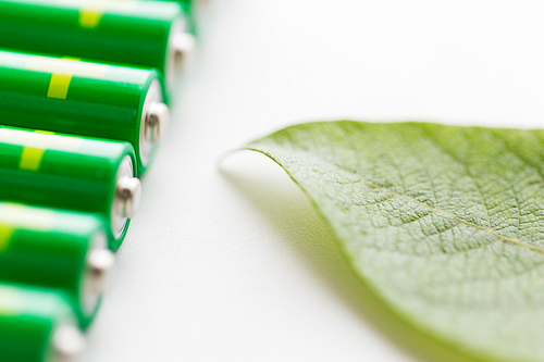 recycling, energy, power, environment and ecology concept - close up of green alkaline batteries and leaf
