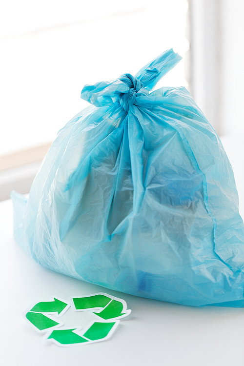 waste recycling, reuse, garbage disposal, environment and ecology concept - close up of rubbish bag with trash or garbage and green recycle symbol at home