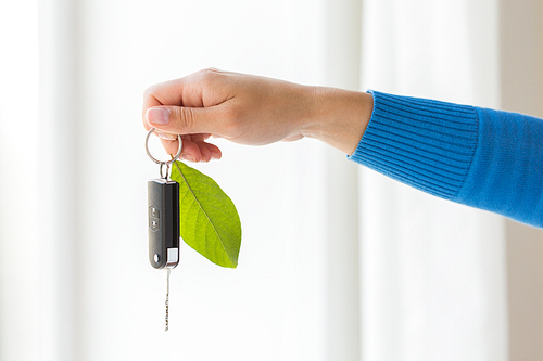 conservation, environment, people, transport and ecology concept - close up of hand holding car key with green leaf trinket
