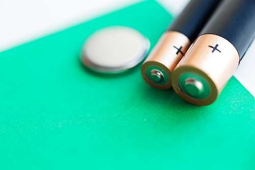 recycling, energy, power, environment and ecology concept - close up of alkaline batteries and green blank copy space