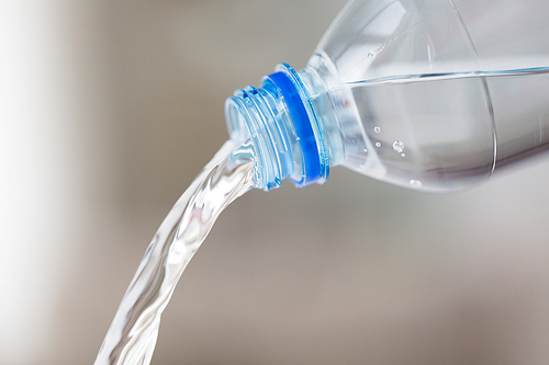 , healthy eating and food storage concept - close up of water pouring from plastic bottle