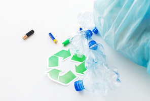 waste recycling, reuse, garbage disposal, environment and ecology concept - close up of used crashed plastic water bottles and batteries with rubbish bag and green recycle symbol