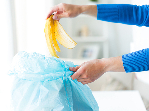 recycling, food waste, garbage, environment and ecology concept - close up of hand putting banana peel into rubbish bag at home