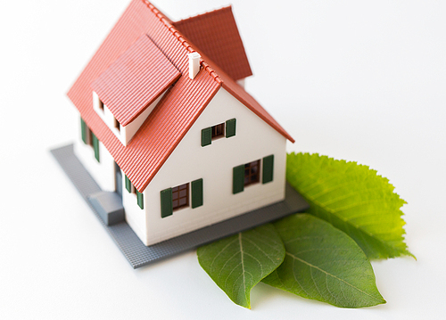 housing, environment and ecology concept - close up of living house model and green leaves