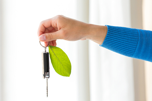 conservation, environment, people, transport and ecology concept - close up of hand holding car key with green leaf trinket