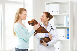 medicine, pet care and people concept - happy woman and veterinarian doctor holding dachshund dog at vet clinic