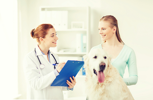 medicine, pet, animals, health care and people concept - happy woman with golden retriever dog and veterinarian doctor writing to clipboard at vet clinic
