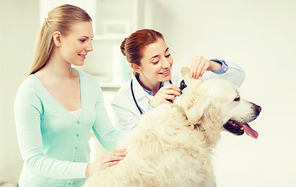 medicine, pet, animals, health care and people concept - happy woman and veterinarian doctor with otoscope checking up golden retriever dog ear at vet clinic
