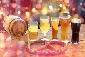 brewery, drinks and food concept - close up of different beer glasses, wooden barrel and pretzel on table over holidays lights background