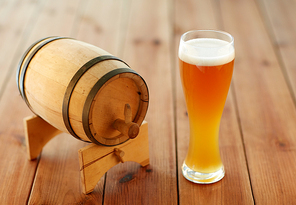 brewery, drinks and alcohol concept - close up of draft lager beer in glass and wooden barrel on table