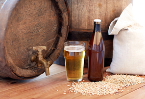 brewery, drinks and alcohol concept - close up of old beer barrel, glass, bottle and bag with malt on wooden table