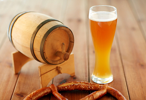 brewery, drinks and alcohol concept - close up of draft lager beer in glass, pretzel and wooden barrel on table