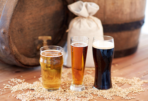 brewery, drinks and alcohol concept - close up of old beer barrel, glasses and bag with malt on wooden table