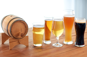 brewery, drinks and alcohol concept - close up of different beers in glasses and barrel on table