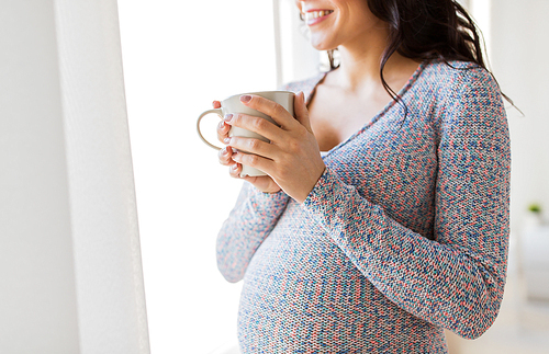 pregnancy, drinks, rest, people and expectation concept - close up of happy pregnant woman with cup drinking tea looking through window at home