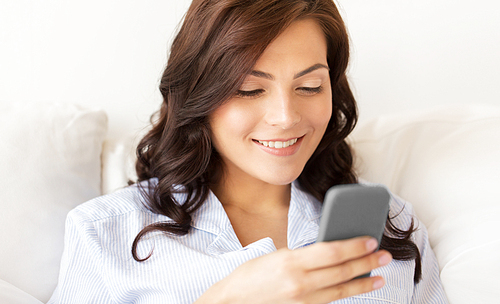 people, technology, communication and leisure concept - happy young woman with smartphone at home