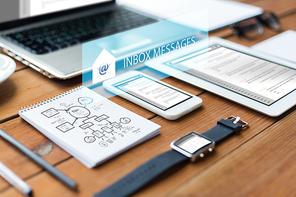 business, internet and technology concept - close up of laptop computer, tablet pc, notebook and smartphone with scheme and inbox messages on wooden table