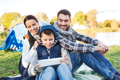 camping, tourism, hike, technology and people concept - happy family with tablet pc computer and tent at camp site