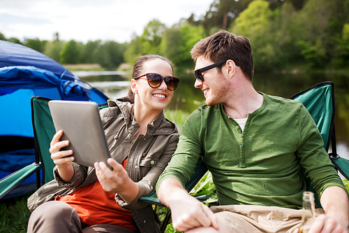 travel, hiking, technology, tourism and people concept - smiling couple with tablet pc computer sitting on chairs at camping tent