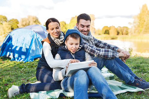 camping, tourism, hike, technology and people concept - happy family with tablet pc computer and tent at camp site